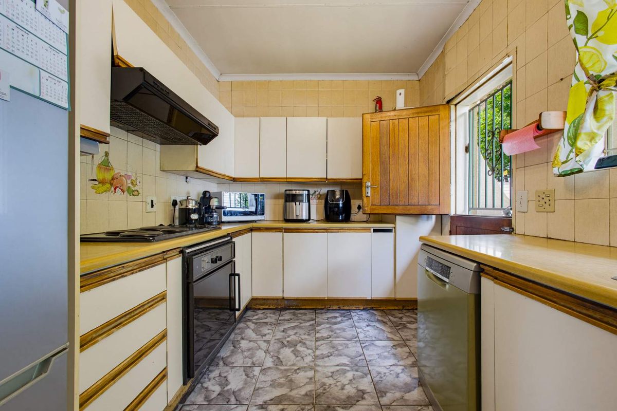 A functional kitchen featuring built-in cabinetry, laminate countertops, and tiled finishes, offering a practical layout with integrated cooking appliances and a window security gate.