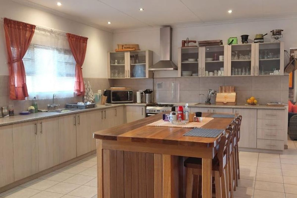 Spacious kitchen featuring light wood cabinetry, a central wooden island with breakfast bar seating, tiled flooring, and integrated stainless steel extractor fan.
