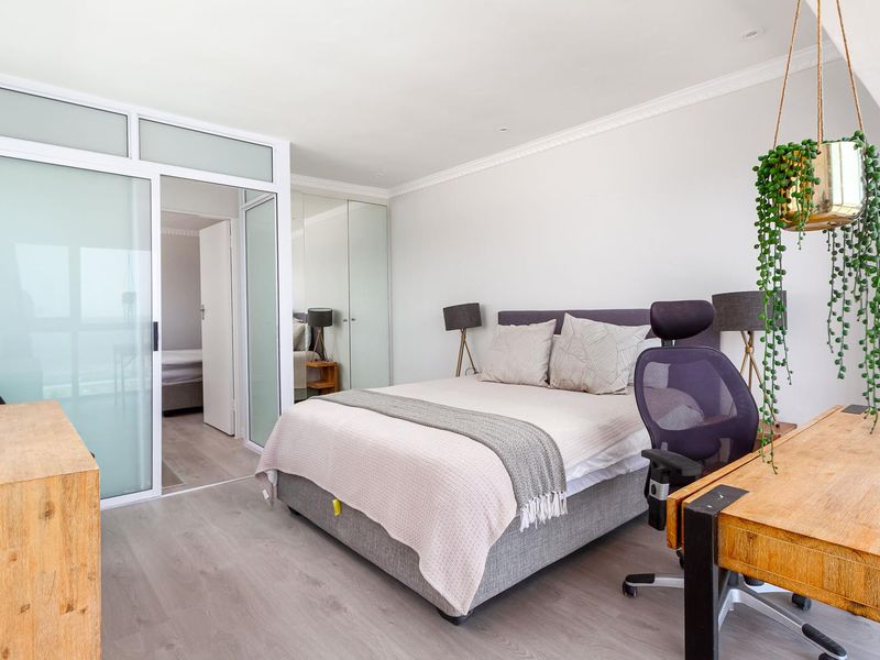 A bright bedroom featuring laminate flooring, mirrored built-in cupboards, and a modern sliding glass partition leading to an adjacent space.