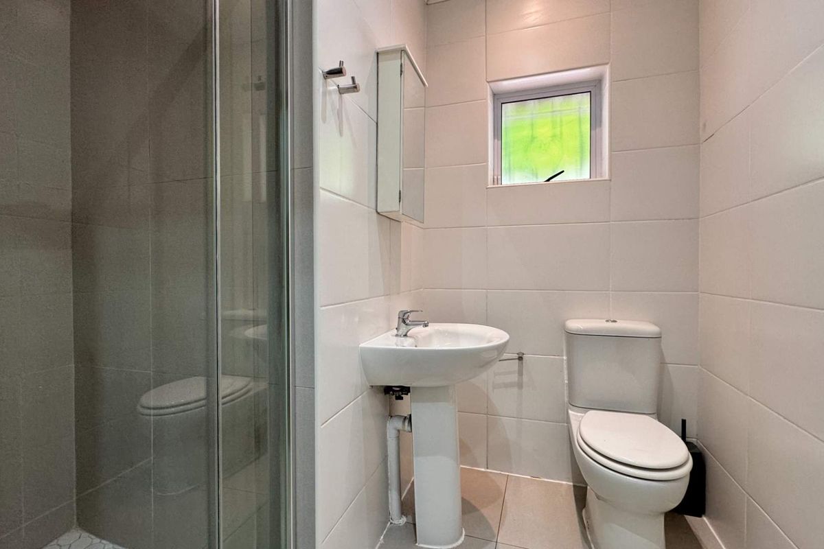A functional bathroom featuring a pedestal basin, toilet, and a glass-enclosed shower with neutral wall and floor tiling.