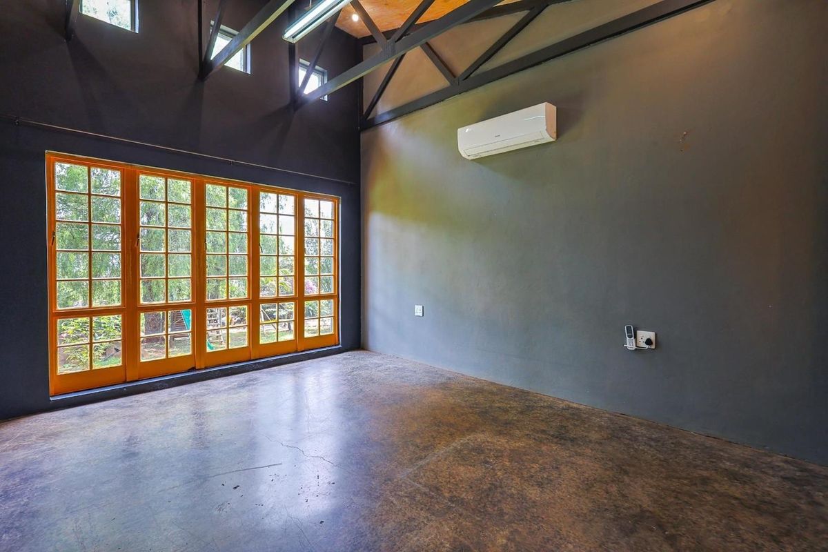Spacious living area featuring high vaulted ceilings with exposed trusses, polished concrete floors, and large wooden-framed glass doors opening to the garden.