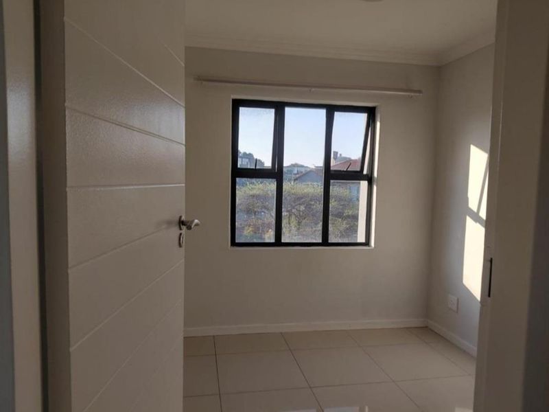 A bright, empty bedroom featuring neutral tiled flooring and a modern aluminium-framed window, offering a clean and versatile space ready for furnishing.