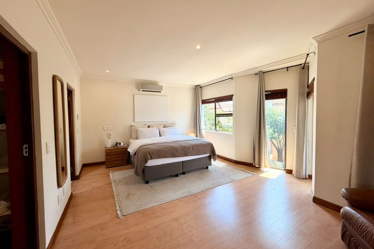 Spacious bedroom featuring laminate flooring, an air conditioning unit, and direct access to the outdoors via a sliding door.