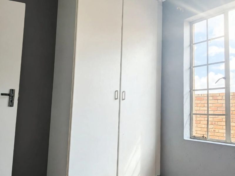 A bright, empty bedroom featuring laminate flooring, a built-in wardrobe, and a grid-pattern window with natural light.