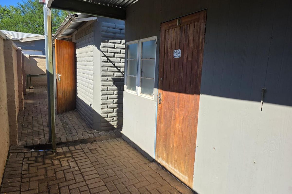 Exterior view of a side entrance featuring a paved walkway, timber door, and corrugated metal roofing structure.