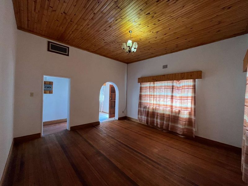 An empty living room featuring hardwood flooring, a timber tongue and groove ceiling, and a classic arched doorway leading to adjacent spaces.