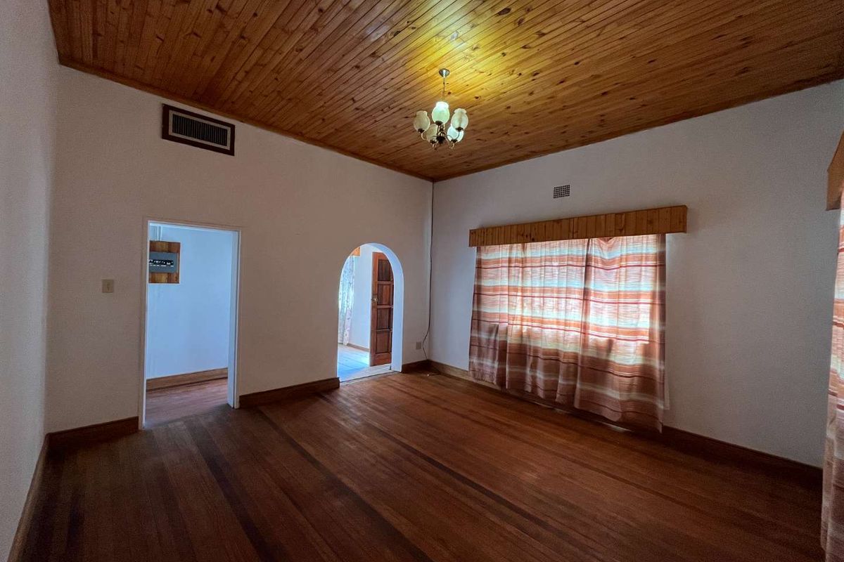 An empty living room featuring hardwood flooring, a timber tongue and groove ceiling, and a classic arched doorway leading to adjacent spaces.