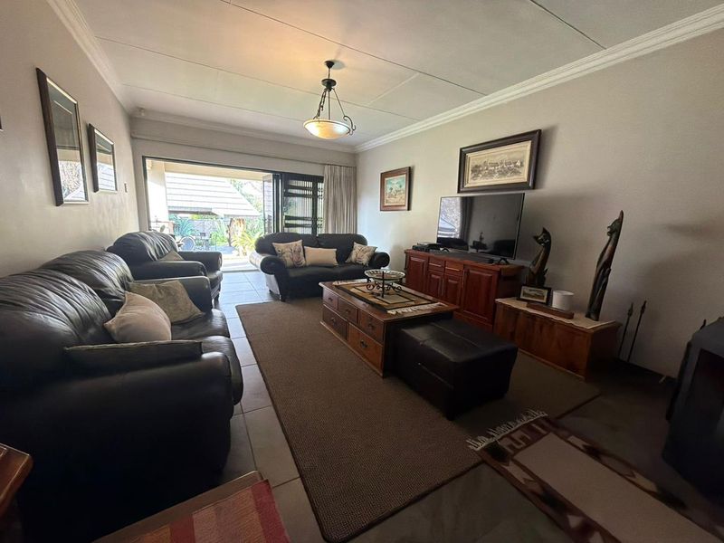 A comfortable living room featuring tiled flooring, crown molding, and a large sliding glass door providing direct access to the outdoor patio area.