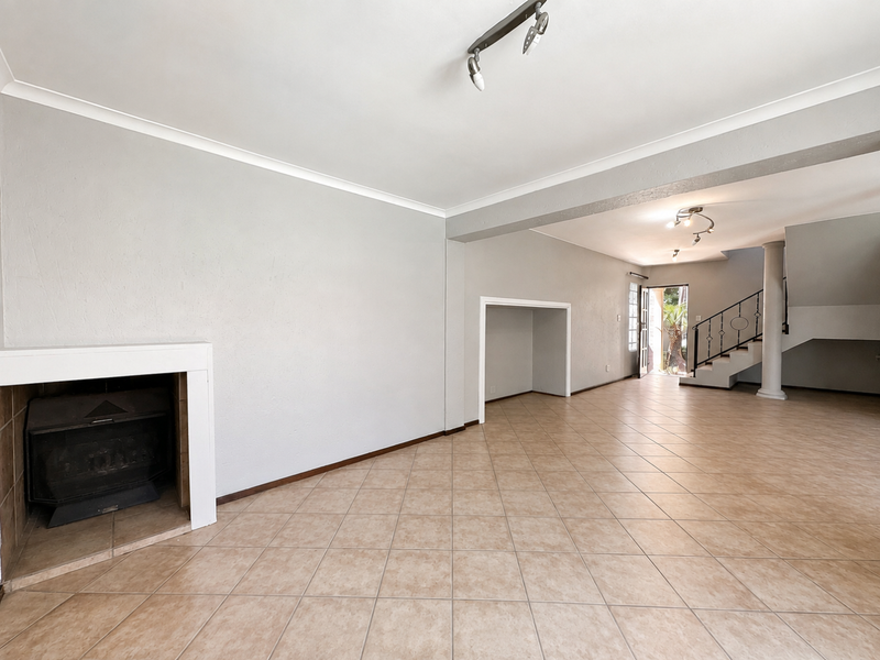 Spacious open-plan living area featuring tiled flooring, a built-in fireplace, and a staircase with a decorative wrought iron balustrade.