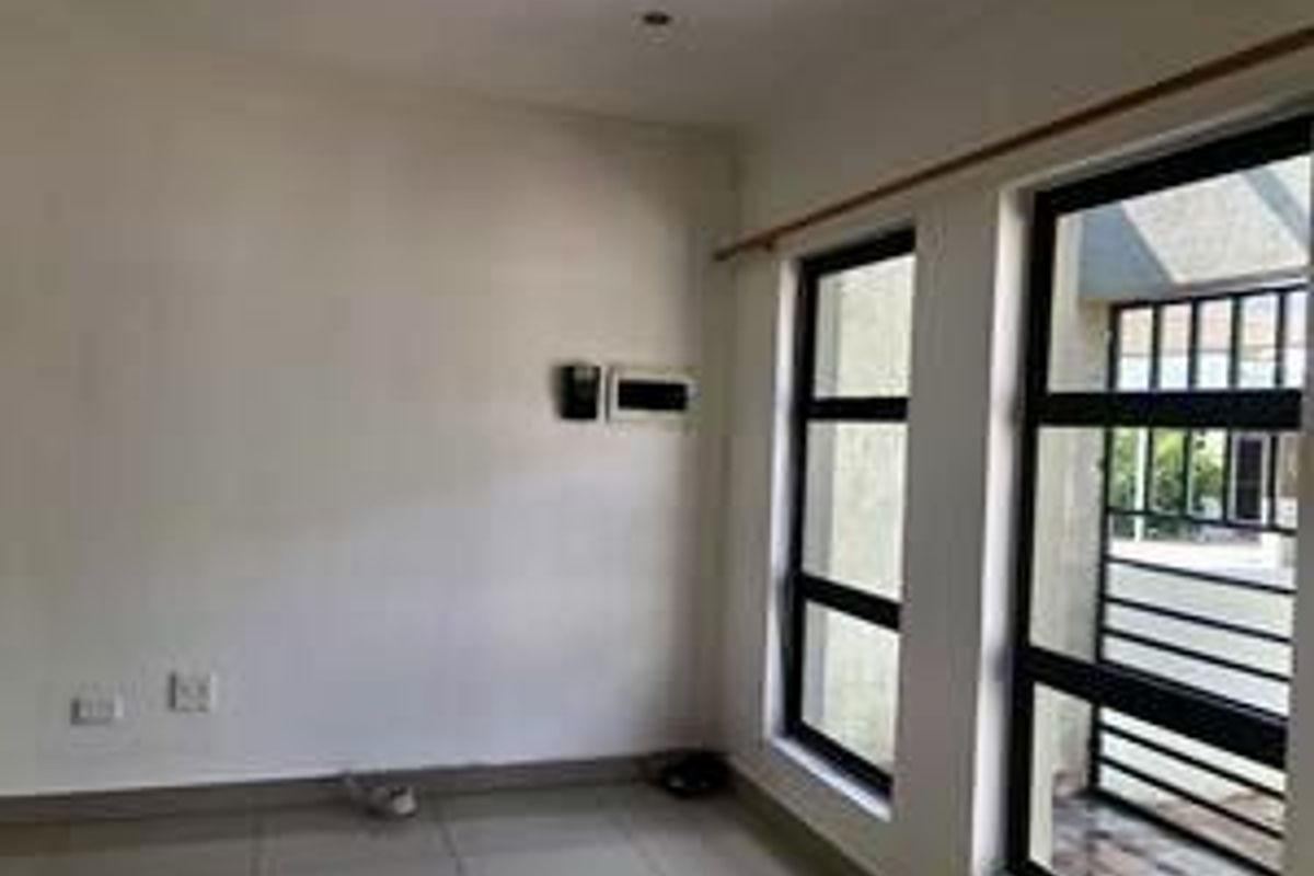 A bright, empty living area featuring large windows with security bars, tiled flooring, and neutral wall finishes.