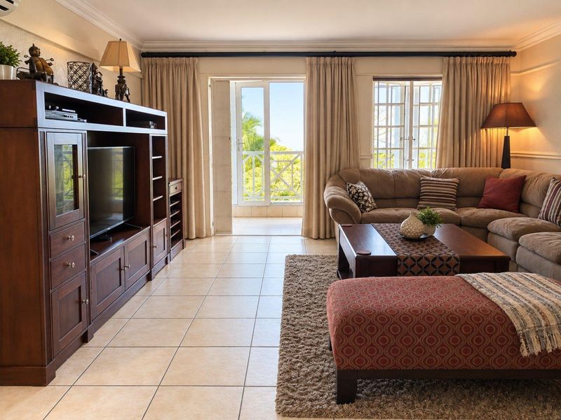 A well-maintained living room featuring tiled flooring, crown molding, and direct access to a balcony through a glass-paneled door.