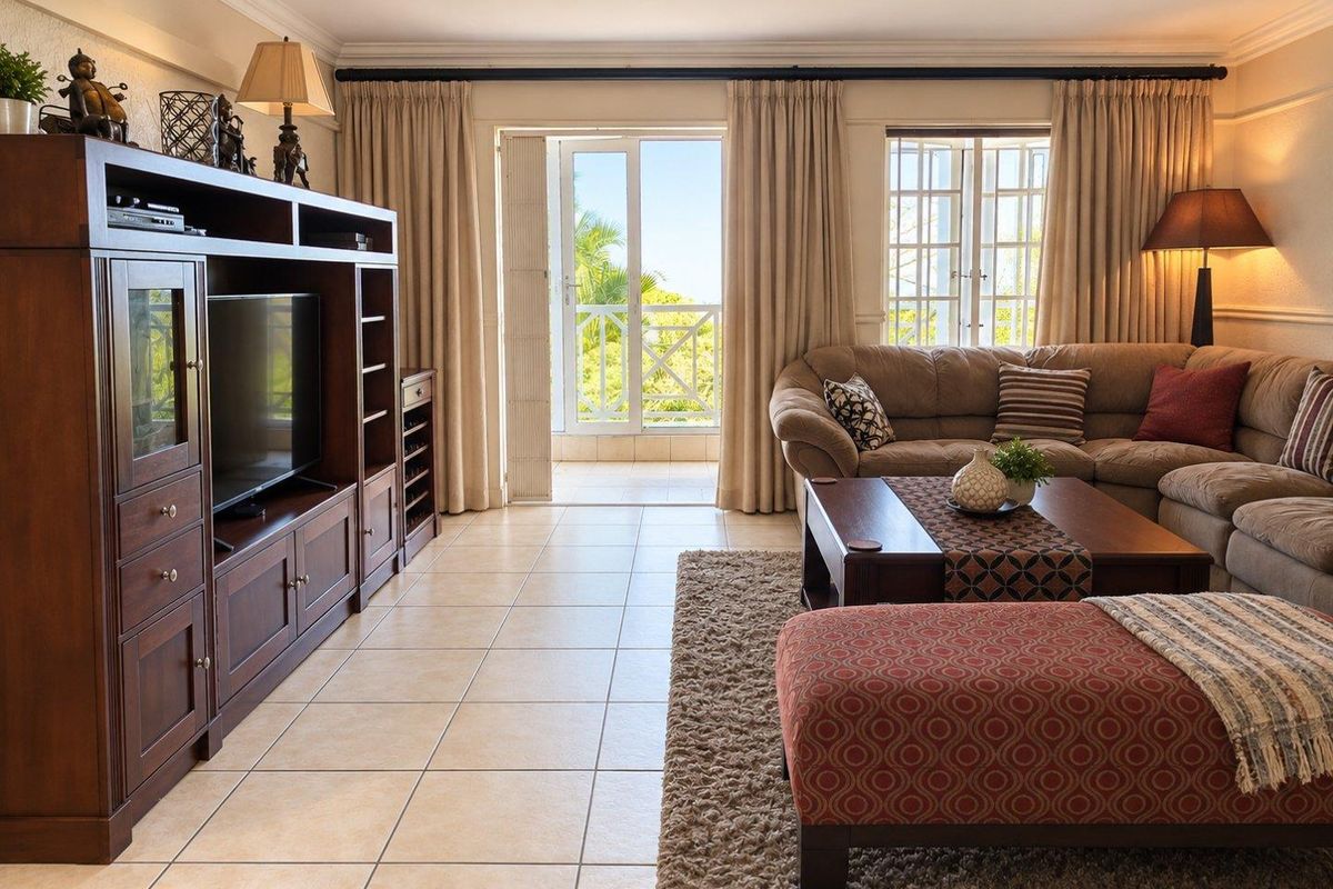 A well-maintained living room featuring tiled flooring, crown molding, and direct access to a balcony through a glass-paneled door.