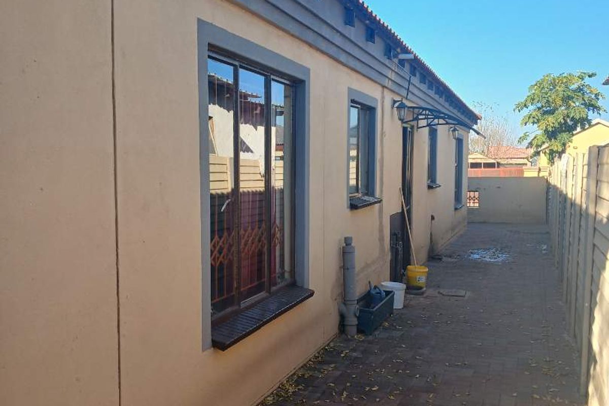 Side exterior view of the property featuring paved walkway, security bars on windows, and perimeter walling.