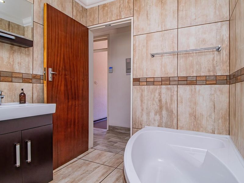 A clean, modern bathroom featuring tiled walls, a corner bathtub, and a vanity cabinet with a basin.