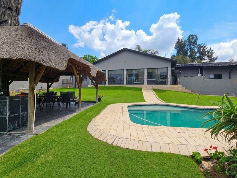 Spacious rear garden featuring a swimming pool, paved surround, and a thatched lapa with a built-in fireplace, perfect for outdoor entertaining.