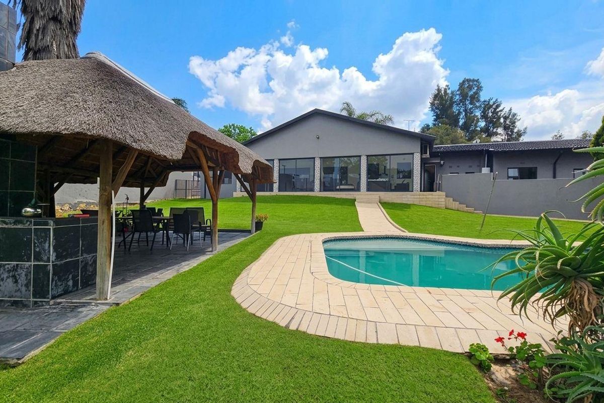 Spacious rear garden featuring a swimming pool, paved surround, and a thatched lapa with a built-in fireplace, perfect for outdoor entertaining.