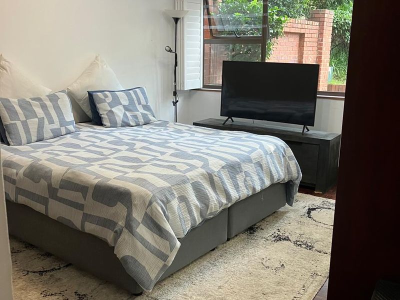 A bedroom featuring parquet flooring and an aluminium window frame, providing a functional space with natural light.