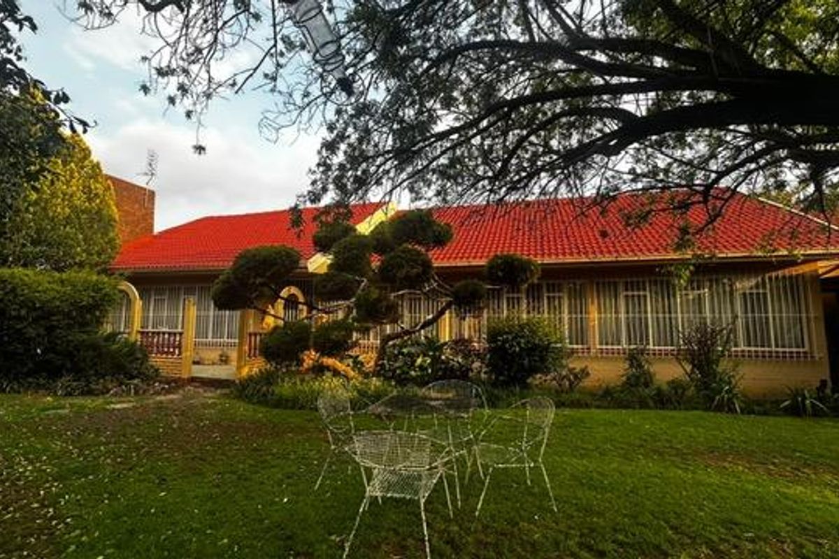 A rear view of the house featuring a red tiled roof, brick exterior, and security bars on the windows, set within a landscaped garden.
