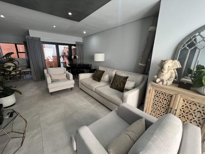 A spacious living room featuring large format floor tiles, a modern recessed ceiling design with downlighting, and sliding glass doors leading to an outdoor area.