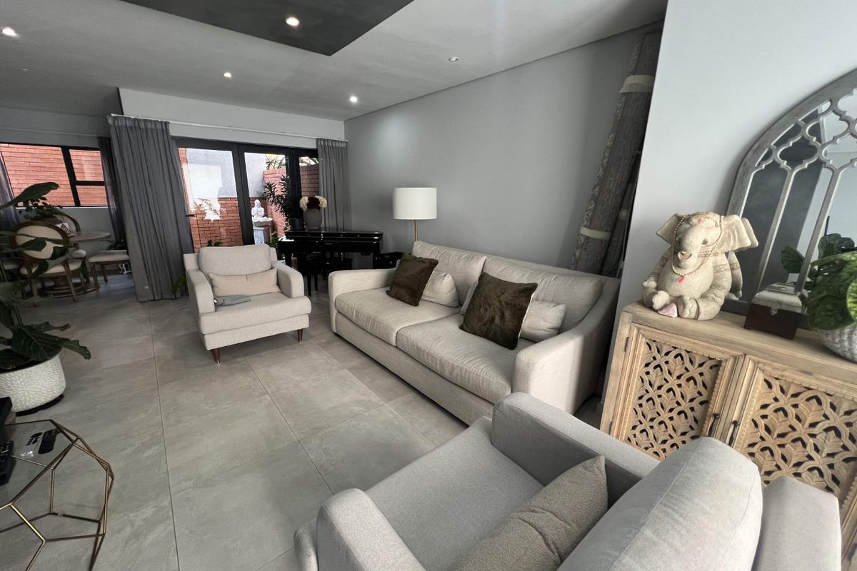 A spacious living room featuring large format floor tiles, a modern recessed ceiling design with downlighting, and sliding glass doors leading to an outdoor area.