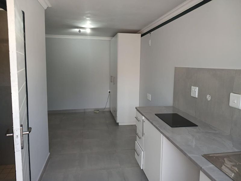 An open-plan studio apartment featuring a modern kitchenette with stone-look countertops, electric hob, built-in cabinetry, and tiled flooring throughout.