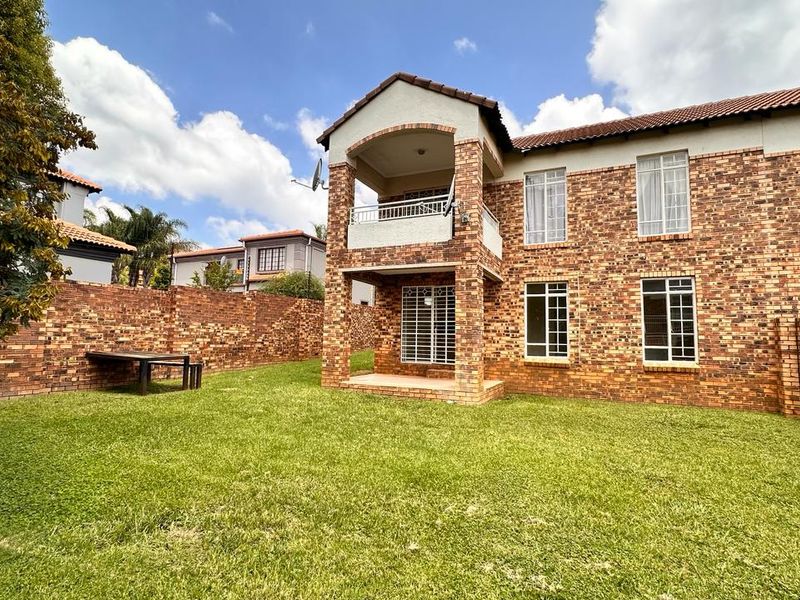 Rear view of a double-story townhouse featuring a face brick exterior, a private balcony, and a spacious grass garden enclosed by brick boundary walls.