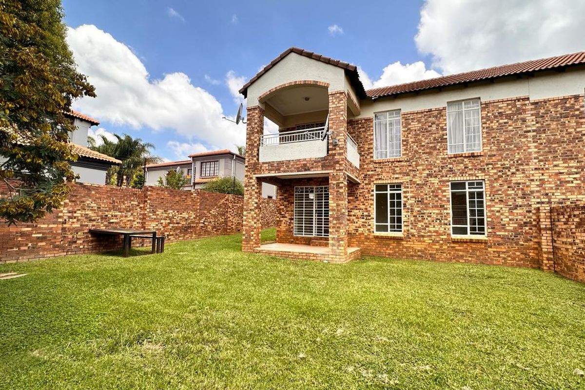 Rear view of a double-story townhouse featuring a face brick exterior, a private balcony, and a spacious grass garden enclosed by brick boundary walls.