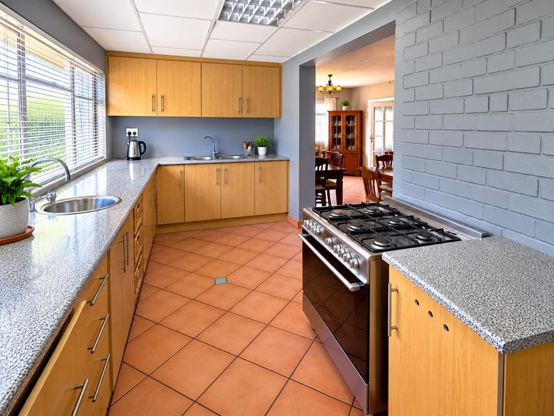 A functional kitchen featuring light wood cabinetry, granite countertops, a stainless steel gas stove, and a distinctive grey painted brick feature wall.