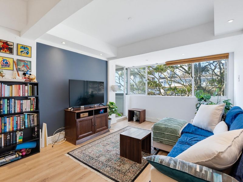 A bright living room featuring laminate flooring, a dark blue accent wall, and large windows providing natural light and a pleasant outlook.
