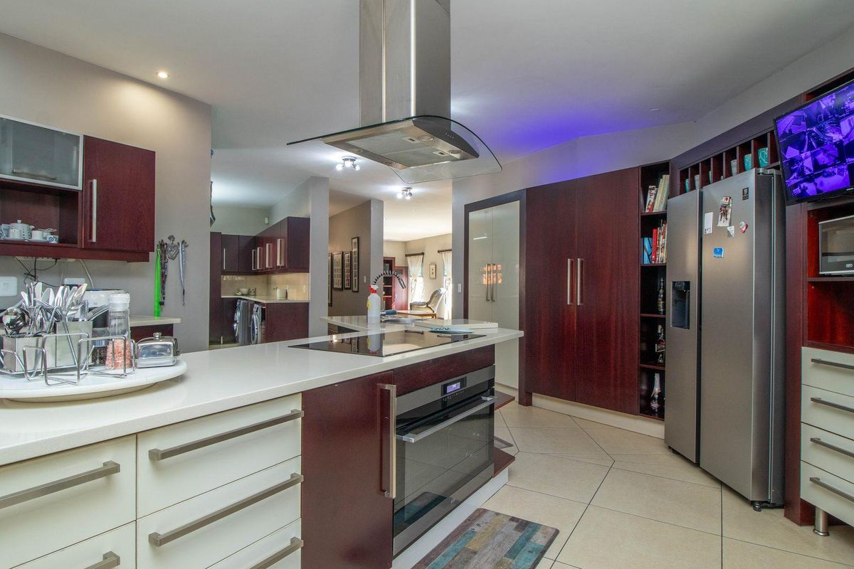 Modern kitchen featuring dark wood cabinetry, stone countertops, a central island with a built-in hob and oven, and a stainless steel extractor fan.