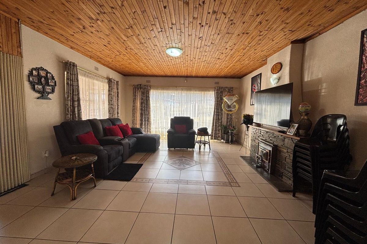 Spacious living room featuring a distinctive timber-clad ceiling, tiled flooring, and a stone-clad fireplace, with large sliding doors providing natural light.