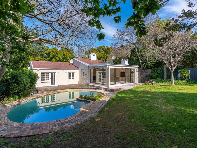 Rear view of the property featuring a swimming pool, wooden decking, and a spacious garden with mature trees.