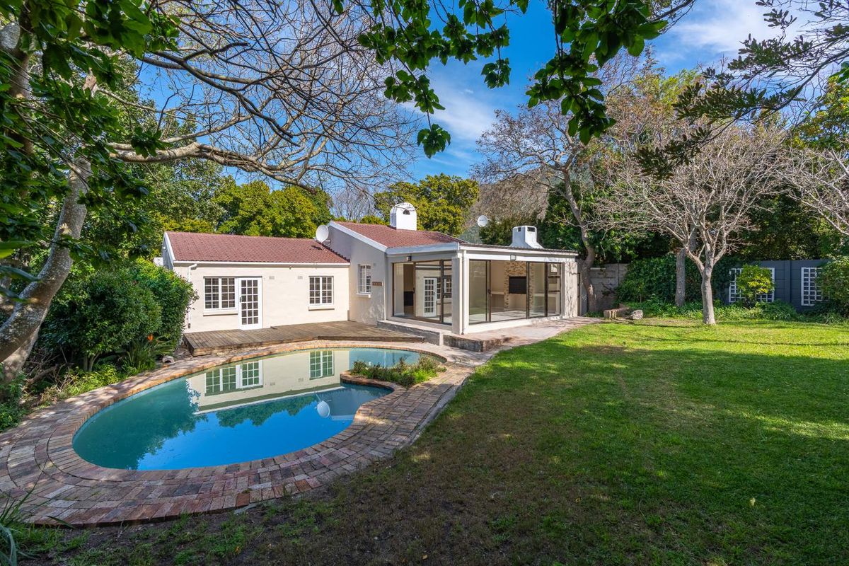 Rear view of the property featuring a swimming pool, wooden decking, and a spacious garden with mature trees.