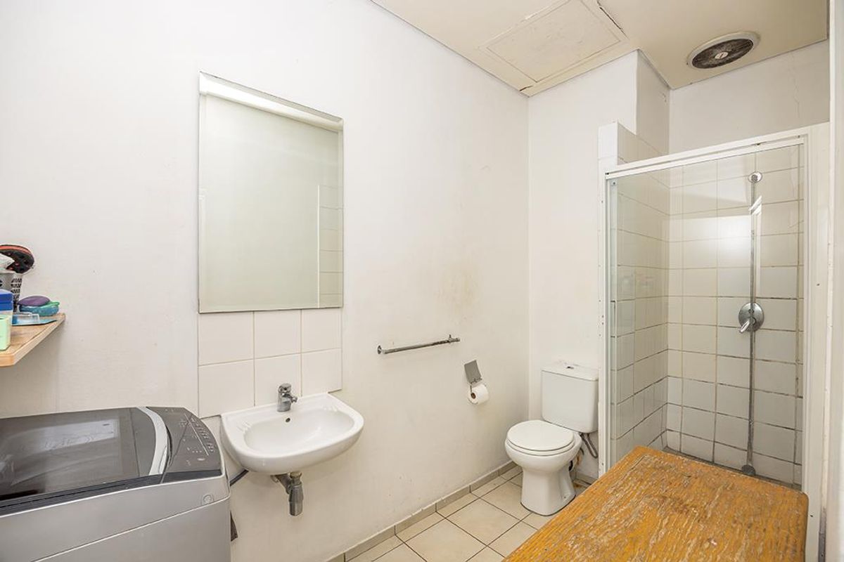 Functional bathroom featuring a shower enclosure, wall-mounted basin, and toilet, with tiled flooring and wall-mounted mirror. Requires cosmetic updates to wall finishes.