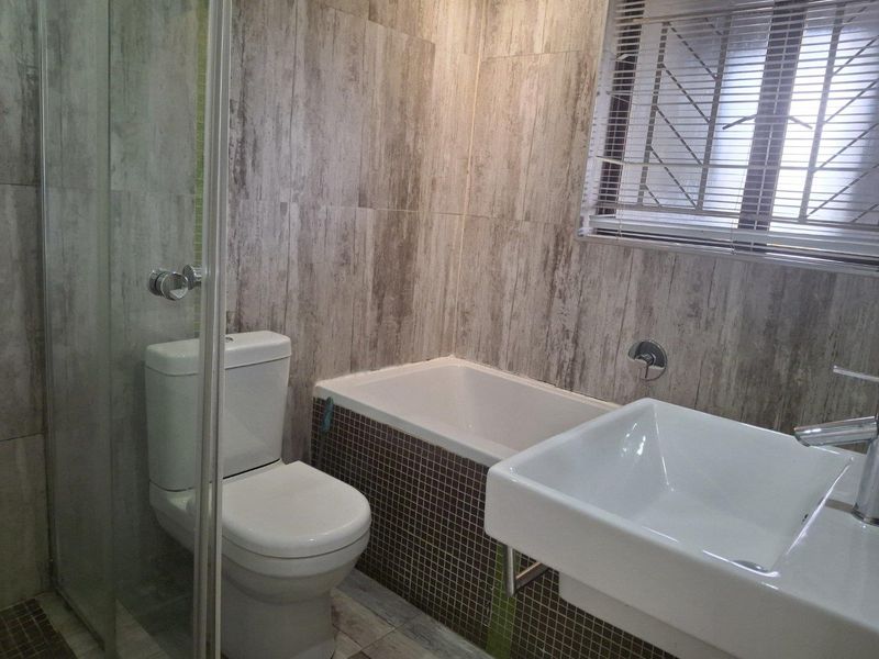 Modern bathroom featuring a shower enclosure, bathtub with mosaic tile surround, wall-mounted basin, and neutral wood-look wall tiling.