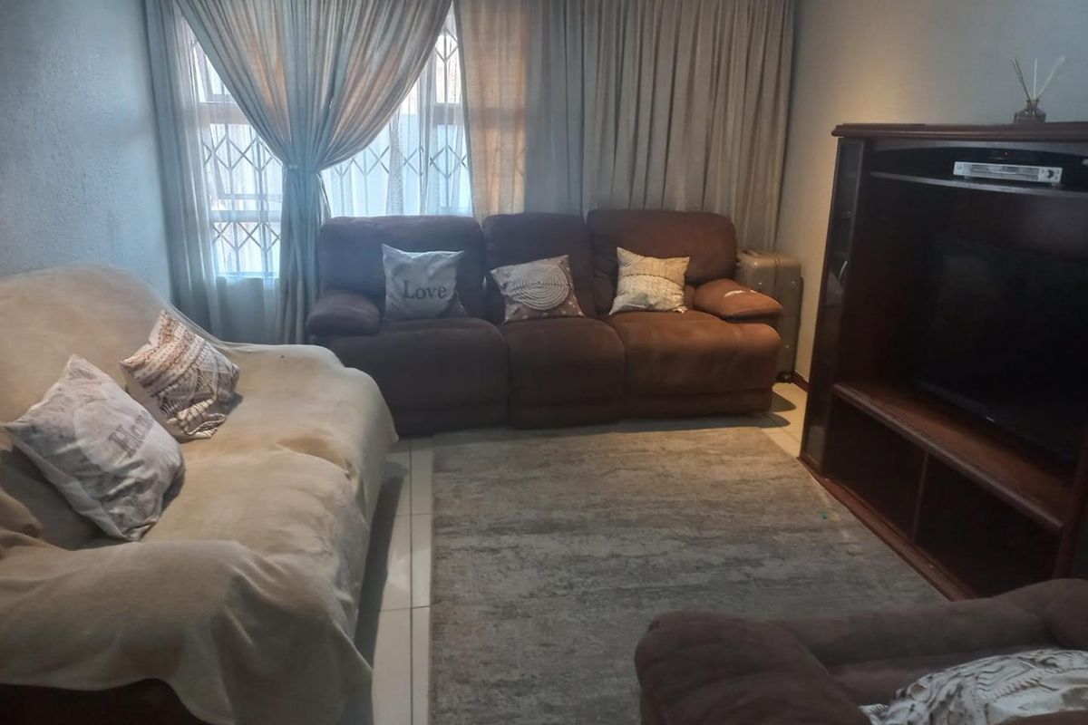 A comfortable living room featuring tiled flooring and large windows with security gates, providing a functional space for relaxation.