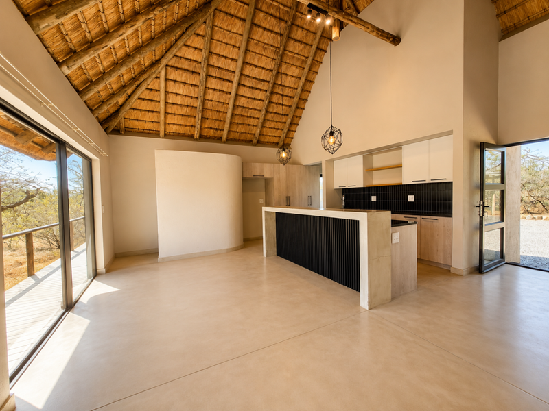 Spacious open-plan kitchen and living area featuring a high thatched ceiling, exposed timber rafters, polished concrete floors, and a modern kitchen island.