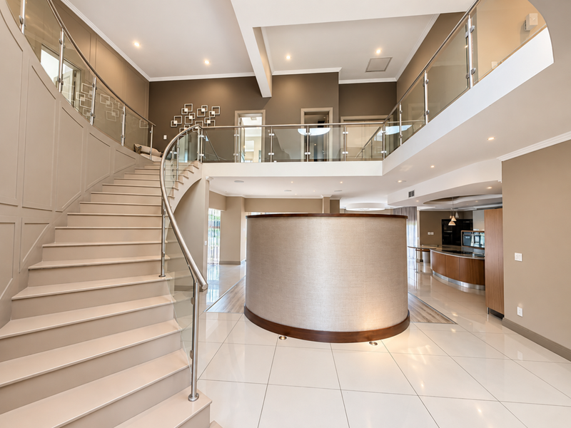 Grand entrance foyer featuring a striking curved staircase with glass balustrades, high ceilings, and a mezzanine level overlooking the open-plan living space.