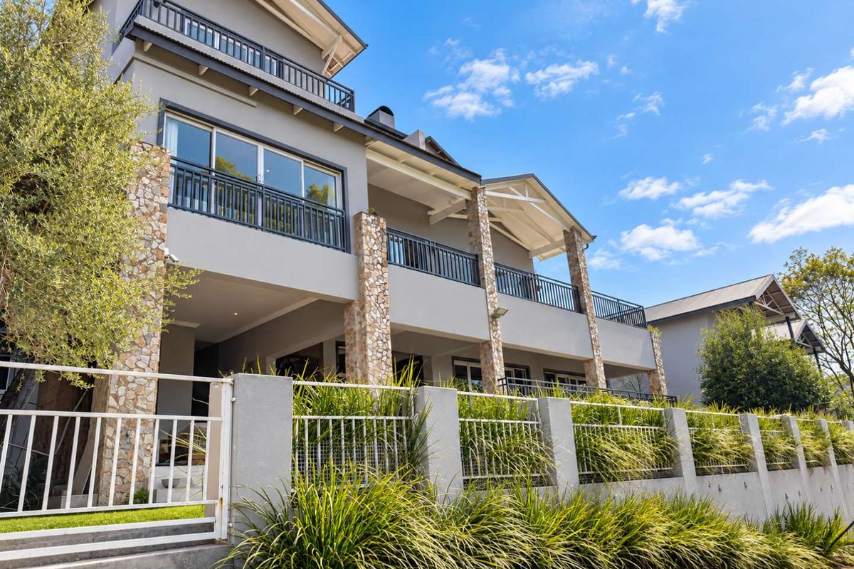 A multi-story residential exterior featuring stone-clad pillars, expansive balconies with metal railings, and well-maintained landscaping behind a secure boundary wall.