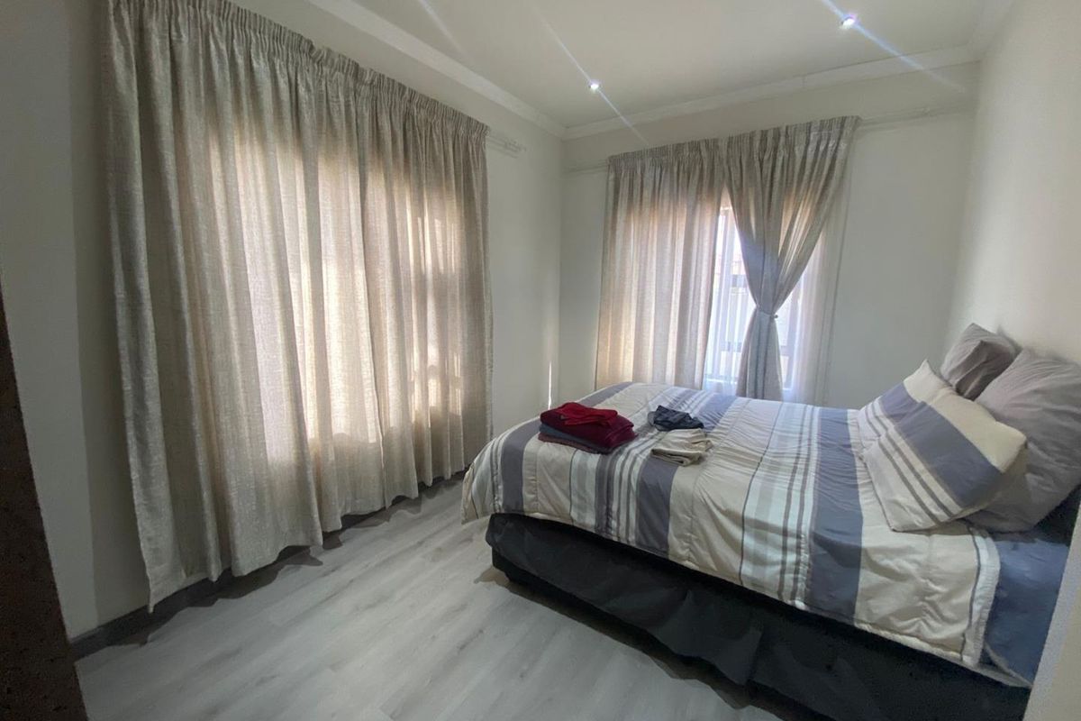 A well-lit bedroom featuring modern light-toned laminate flooring and dual windows with installed curtain tracks.