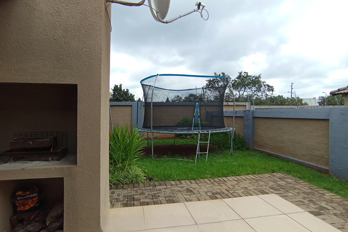 A private rear garden featuring a paved patio area with a built-in brick braai and a grass lawn enclosed by perimeter boundary walls.