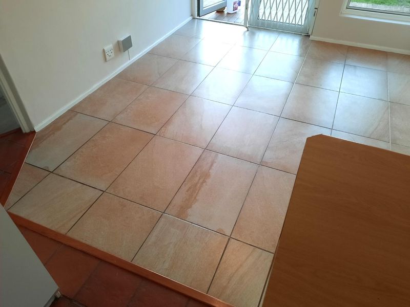 An empty living area featuring neutral ceramic floor tiles, direct access to the exterior via a glass sliding door, and fitted security gate.