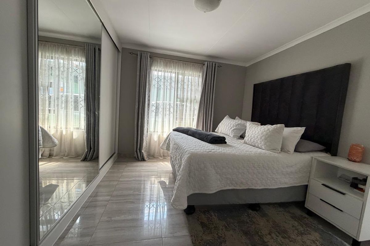 A well-maintained bedroom featuring large format floor tiles, a spacious built-in mirrored wardrobe, and security bars on the window for added peace of mind.