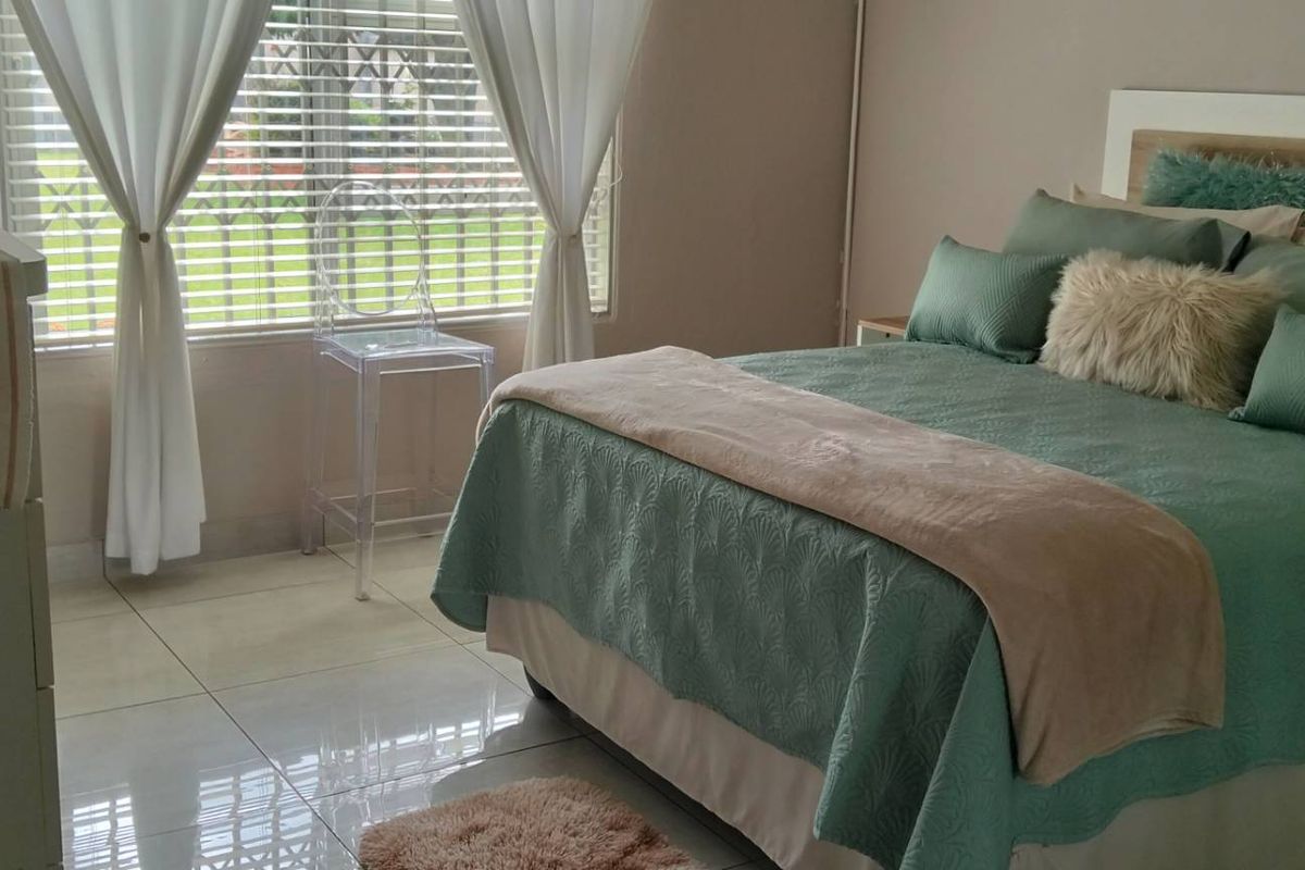 A well-maintained bedroom featuring neutral wall tones, large windows with blinds, and polished floor tiles.