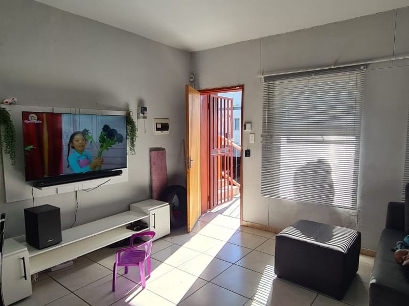 A functional living room featuring tiled flooring, venetian blinds, and direct access to an exterior security gate.