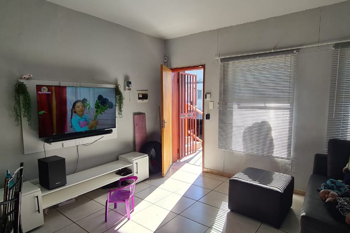 A functional living room featuring tiled flooring, venetian blinds, and direct access to an exterior security gate.