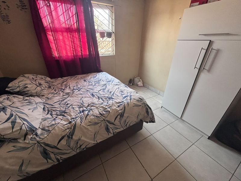 A functional bedroom featuring tiled flooring, a built-in wardrobe, and a window fitted with security bars.