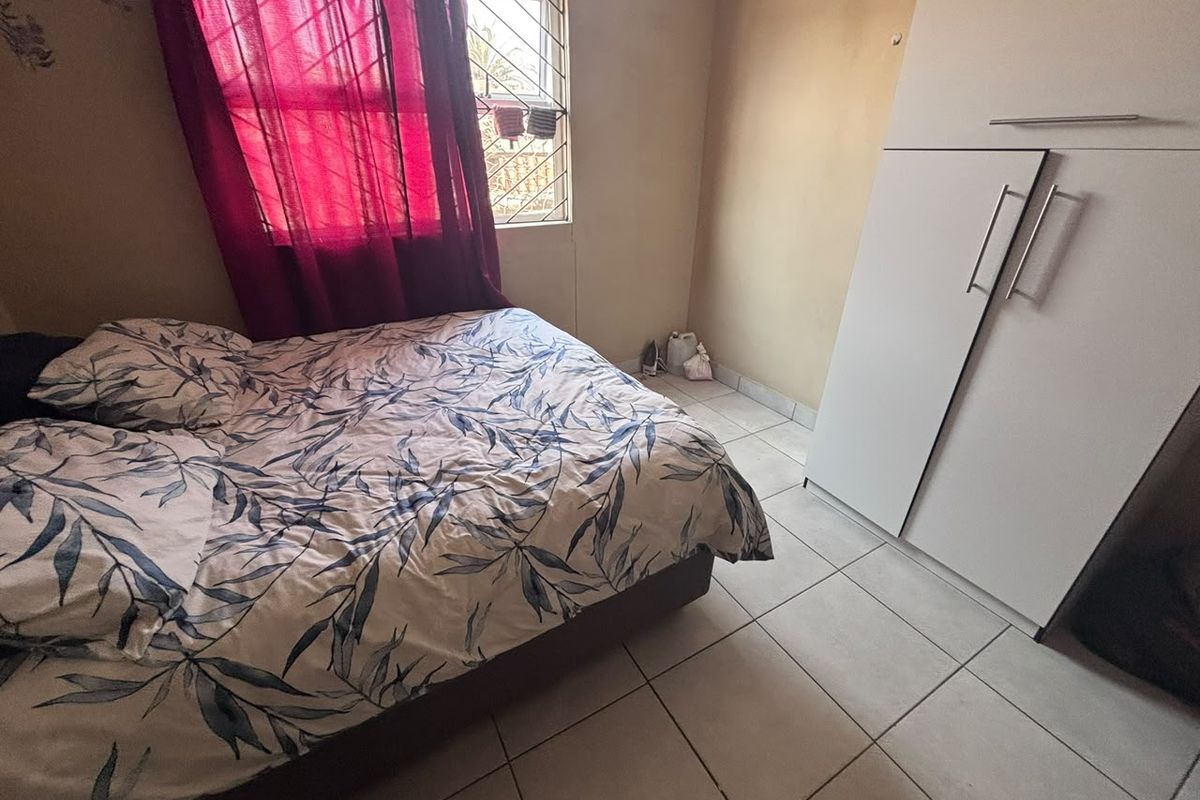 A functional bedroom featuring tiled flooring, a built-in wardrobe, and a window fitted with security bars.