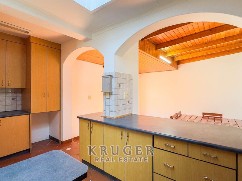 A functional kitchen featuring laminate cabinetry, tiled splashbacks, and an open-plan layout with exposed timber ceiling beams and a skylight.