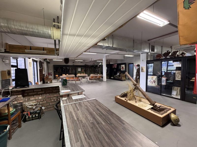 Spacious clubhouse interior featuring industrial-style exposed ducting, concrete flooring, a brick-faced bar counter, and integrated display cabinets for historical exhibits.